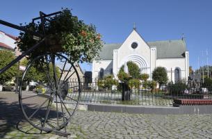 Kościół pw. Świętej Trójcy z zewnątrz. Na pierwszym planie wielki rower stojący na rynku. 